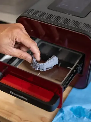 A printed surgical guide being lifted from the 3D printer at the practice.